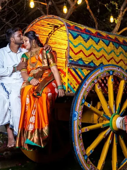 A traditional South Indian pre-wedding shoot. The couple is dressed in classic attire, with her in a beautiful orange silk saree and him in a white veshti.