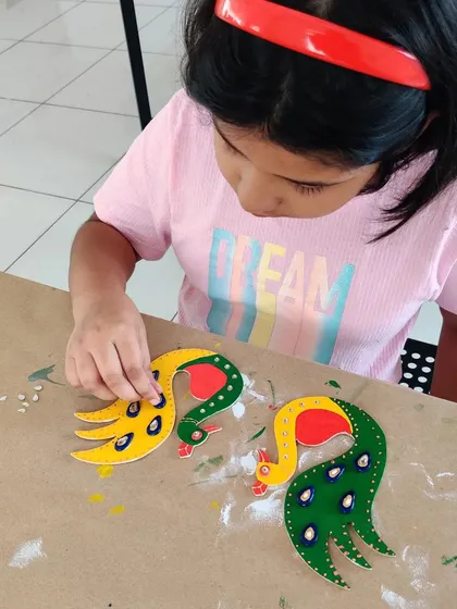 Adding the final touches to her peacock T-light holders. This step involves carefully placing decorative stones, which is a fun way to add sparkle and practice fine motor skills.