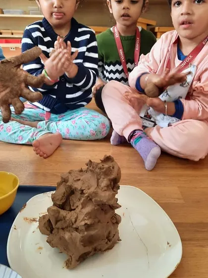 Children watch intently as a teacher demonstrates how to mold the clay. This hands-on experience is a powerful way to learn.