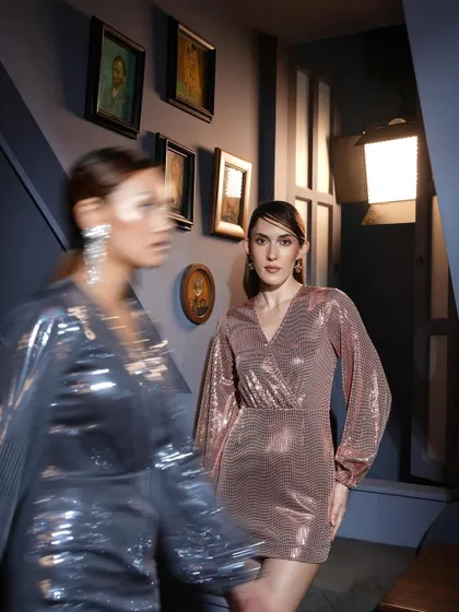An artistic shot using motion blur to capture the energy of a night out. The focus remains on the model in the rose gold dress, creating a dynamic and visually interesting image.