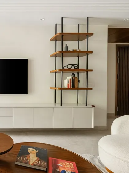 The TV unit combines a sleek white console with a custom open shelving unit. This design provides practical storage while the contrast between the dark metal frame and warm wood shelves adds a modern, graphic element.