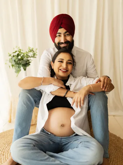 A happy couple in a casual, light-filled setting. The simple white shirts and jeans, paired with the natural decor, create a relaxed and authentic maternity portrait.