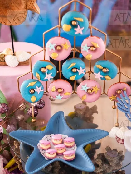 A sweet display of donuts and macarons at a mermaid-themed party. The treats are decorated with starfish and shells, perfectly matching the underwater theme and adding to the visual appeal of the dessert table.