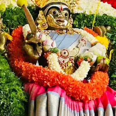 A close-up of a deity adorned with a fresh garland of orange and white flowers, ready for a temple festival.