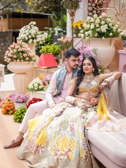 A beautiful shot of the couple amidst a sea of pastel flowers. The decor features large pots filled with roses, chrysanthemums, and other blooms, creating a lush and romantic photo corner.