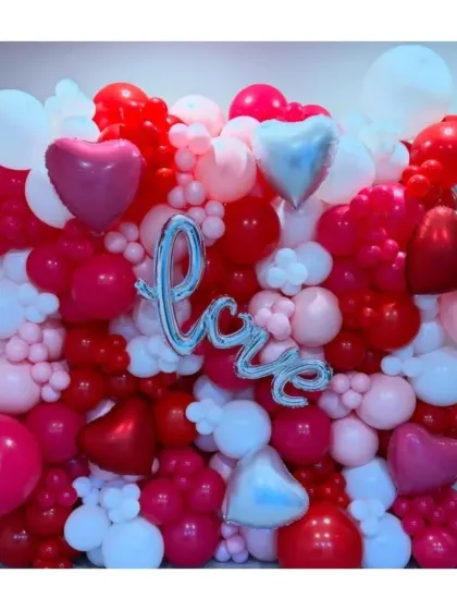 A dense and textured balloon wall in shades of red, pink, and white. The silver "Love" foil balloon and heart accents make this a fun and vibrant backdrop for celebrating love.