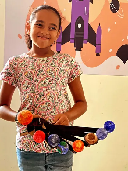 A smiling student proudly presents her colorful, hand-painted model of the solar system.