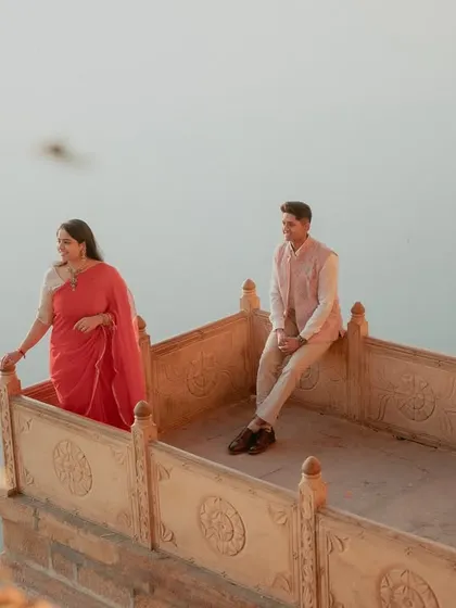 A beautiful shot of a couple on a traditional stone balcony overlooking the water in Jaisalmer. The warm, golden light of the setting sun enhances the romantic and historic feel of the location.