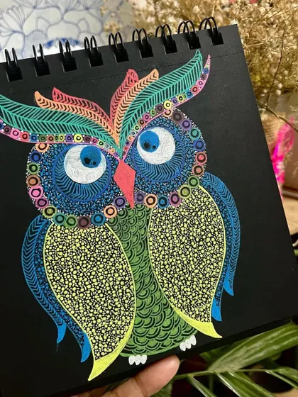 A vibrant owl with detailed feather patterns, created with gel pens on black paper.