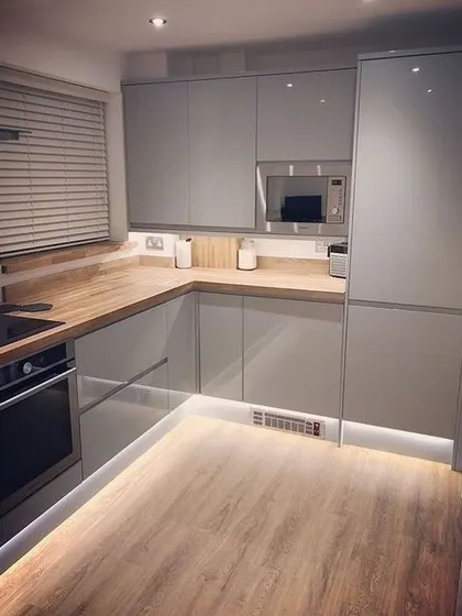 A compact and efficient L-shaped kitchen in a light grey gloss finish with a wood countertop. The toe-kick lighting is a great feature that adds both safety and ambiance.