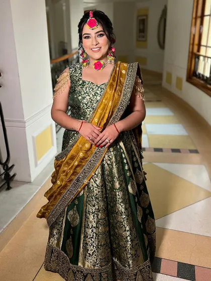 A full-length shot showcasing the bride's stunning Mehendi outfit and her radiant smile. She looks comfortable and happy, ready to get her henna done.