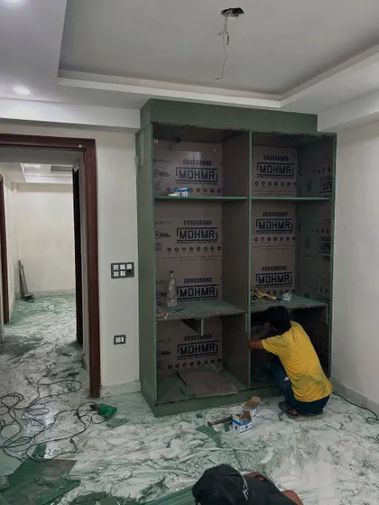 We use high-quality, moisture-resistant green plywood for wardrobes and kitchens to ensure longevity. Here, a carpenter is assembling the frame of a large bedroom wardrobe.
