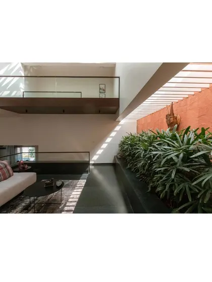 A tranquil seating area in the Notan Home, where a long planter of greenery is bathed in sunlight from a linear skylight above. The textured red wall adds warmth and depth to the space, creating a perfect spot for quiet contemplation.