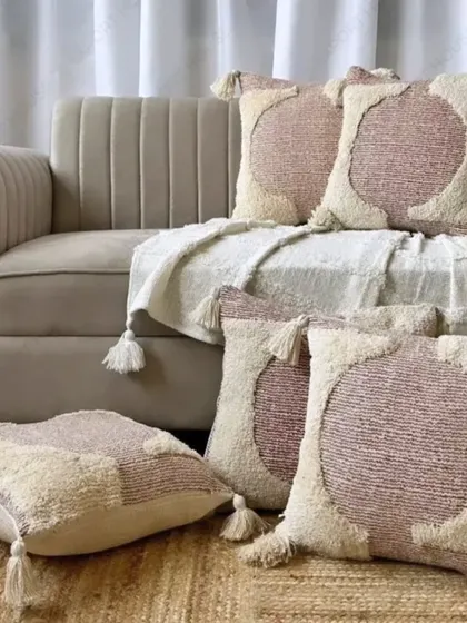 This tufted boho cushion cover features an abstract circular pattern with tassels. The neutral tones make it a versatile piece for any modern or bohemian interior.