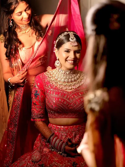 A behind-the-scenes moment of the bride getting ready, smiling in the mirror as her dupatta is adjusted. This captures the anticipation and happiness before the ceremony.