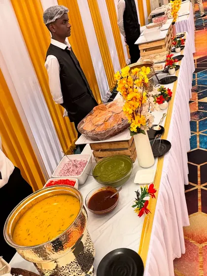 Our staff, dressed in professional uniforms, stand ready at a beautifully decorated buffet. The yellow and white theme with floral accents creates a bright and welcoming atmosphere for guests.