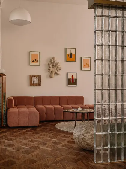 A view of the daughter's bedroom living area, with a plush, channel-tufted sectional sofa, a gallery wall, and a glass block partition that adds a touch of retro glamour.