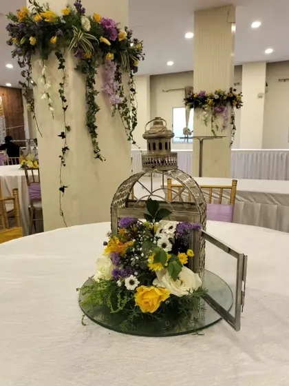 A close-up of a table centerpiece from an anniversary party. The birdcage filled with yellow and white flowers adds a touch of vintage charm and whimsy to the decor.