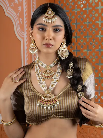 This look captures the complete royal aesthetic, from the layered necklaces to the statement maang tikka and braid accessories, all part of our bridal collection.