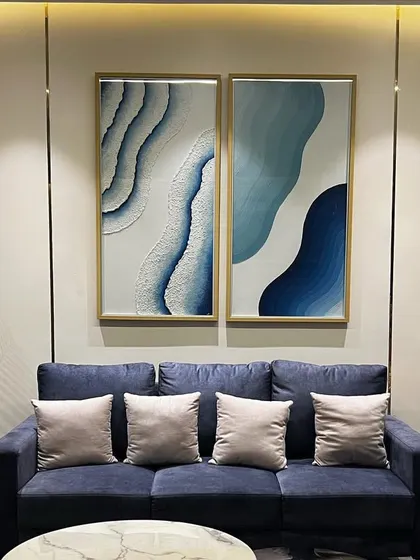 A close-up of the seating arrangement in the Noida project, showing the interplay of colors and textures. The deep blue sofa is paired with neutral cushions, and the abstract wall art ties the color scheme together, creating a harmonious and visually engaging living area.