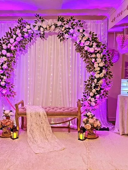 A romantic and dreamy indoor setup for an engagement or Mehendi. The decor features a large floral ring arch with white flowers, set against a backdrop of fairy lights and white curtains, creating a magical and ethereal ambiance.