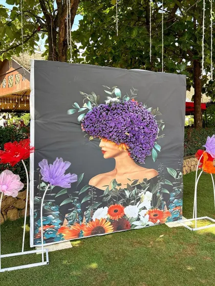 An artistic photo backdrop featuring a portrait made of fresh purple flowers, surrounded by giant paper flowers.