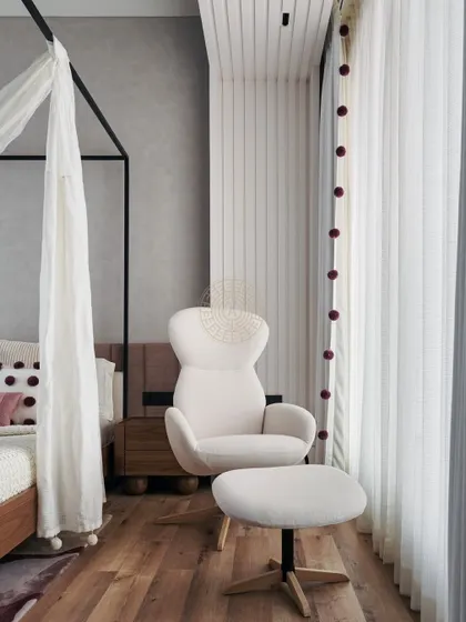 A cozy reading nook by the window, with a comfortable white armchair and ottoman. The pom-pom detail on the curtains adds a playful touch to this elegant bedroom.