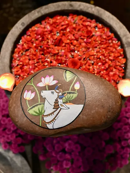 A hand-painted stone with a Pichwai cow, part of a festive display with an uruli and flowers. This is how I love to style my pieces for celebrations, inspired by the rich traditions of our past.