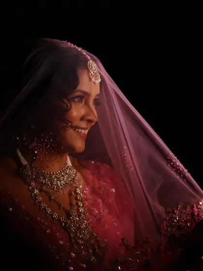 A classic bridal portrait under the veil. The soft lighting and her gentle smile are enhanced by a makeup look that is all about natural radiance and timeless elegance.