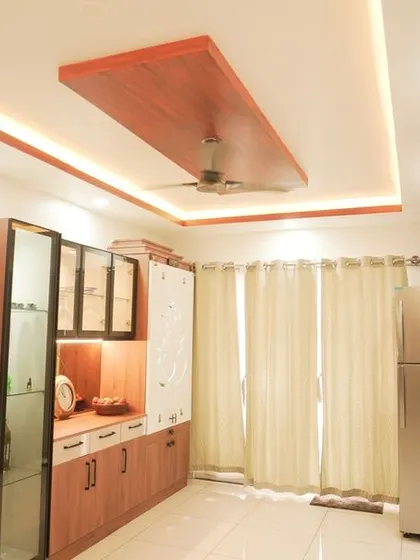 A dining area featuring a large crockery unit with a CNC-cut pooja door. The wooden and white finishes are complemented by a modern false ceiling with wood accents.