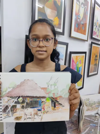 A young artist proudly shows her colored pencil drawing of a rural village scene, a piece that tells a story through its composition.