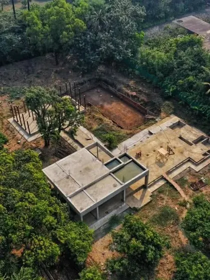 An aerial drone shot showing the foundation and plinth work for the Awas House. The layout is carefully planned to navigate the existing trees and natural contours of the land.