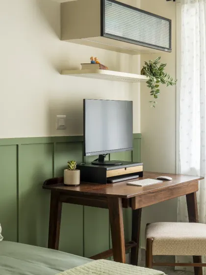 A stylish and compact study unit in dark wood, set against a green paneled wall. The design includes a floating shelf and a wall-mounted cabinet with fluted glass for extra storage.