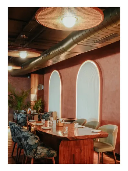 A private dining area is defined by a long, live-edge wooden table and plush, patterned chairs. The moody lighting and arched wall details create a sophisticated and exclusive feel.