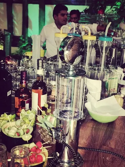A wide view of a busy bar at a large event, featuring a gas pump-style drink dispenser and our team serving a crowd. This highlights our capacity for large-scale beverage catering.