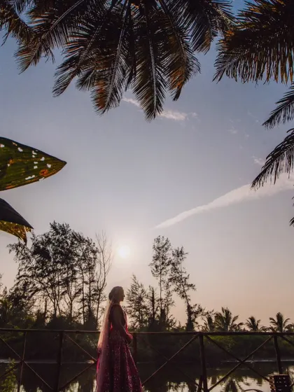 A bride silhouetted against the sunset at a beautiful Goa resort, surrounded by palm trees.