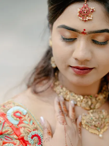 A serene close-up of a bride with her eyes closed, showcasing her intricate makeup, jewelry, and the mehndi on her hands.