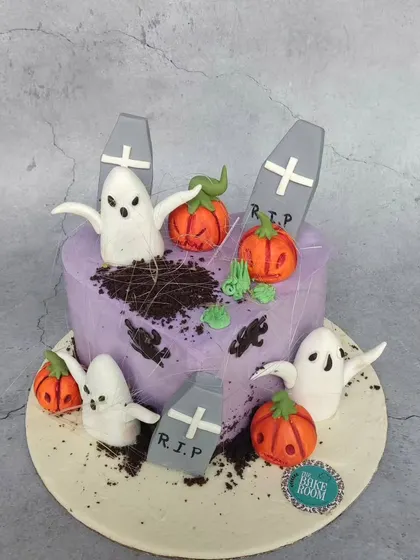 A spooky and fun Halloween cake featuring a graveyard scene. It has edible ghosts, pumpkins, and tombstones, with cookie crumble 'dirt' for a realistic effect.
