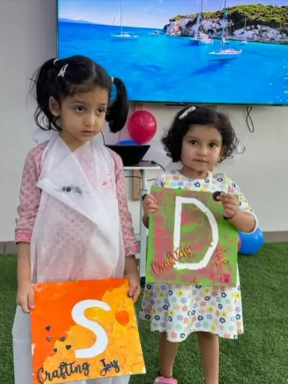 Two young artists proudly holding up their initial paintings from the 'Palette Harmony' workshop. It's wonderful to see their unique creations and the pride on their faces.