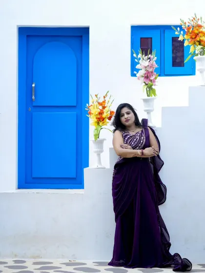 A full-length portrait showcasing a beautiful purple saree against the contrasting white and blue backdrop.