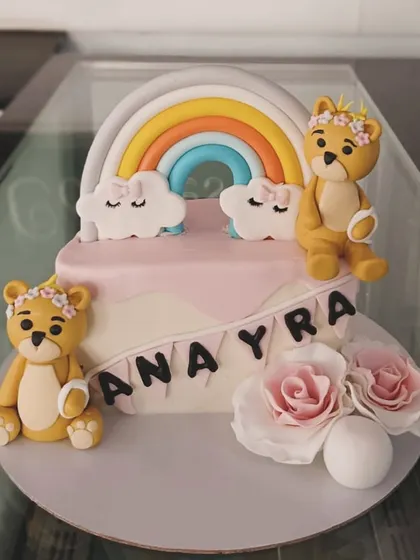 A beautiful cake featuring two teddy bears, a rainbow, and fondant roses. The soft pastel colors make this a perfect choice for a baby shower or first birthday.