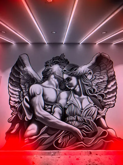 The final angelic couple mural, illuminated by dramatic red lighting. The monochrome painting style allows it to be transformed by colored lights, changing the mood of the room.