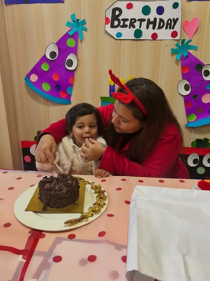 A mother helps her daughter, the birthday girl, take the first bite of her cake.