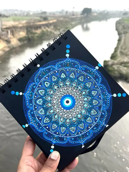 My popular Evil Eye mandala, a symbol of protection, held against a serene river backdrop.