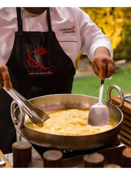 A chef preparing a large batch of Jalebi Rabri, a classic Indian dessert, in a traditional kadai at a live station.