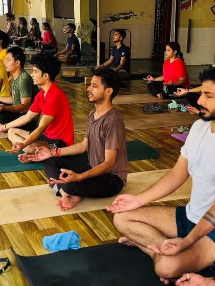 A full class of students sits in Padmasana (Lotus Pose) for meditation. The shared energy in the room enhances the experience, creating a powerful atmosphere of collective calm.