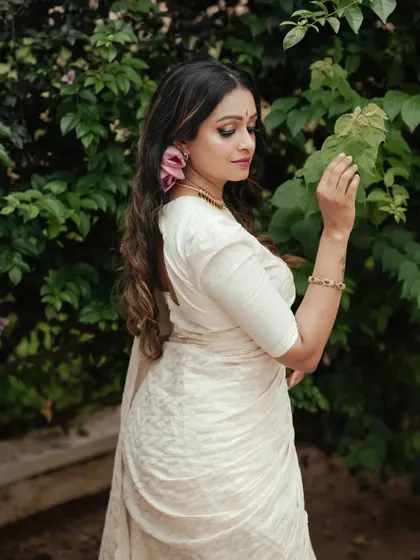 A side profile from the Onam series, highlighting the elegant drape of the saree and the intricate details of her hair and jewelry. The natural setting adds a soft, organic feel.