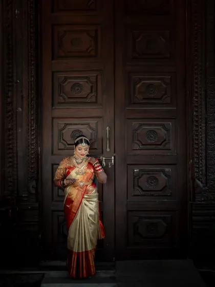 A bride standing before a grand, traditional wooden door. The scale of the door and the rich textures create a sense of history and timeless elegance.