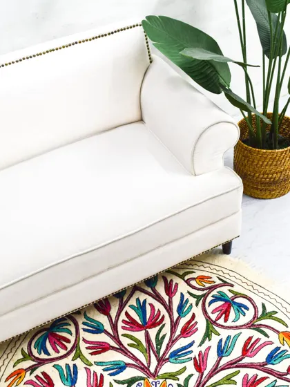 A classic white sofa with elegant rolled arms and nail-head trim detailing along the frame. This timeless piece is paired with a colorful hand-embroidered rug.