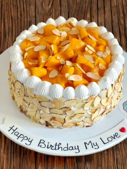 A fresh mango cake with the sides covered in toasted almonds. The combination of sweet mango, light cream, and crunchy nuts is a perfect treat.